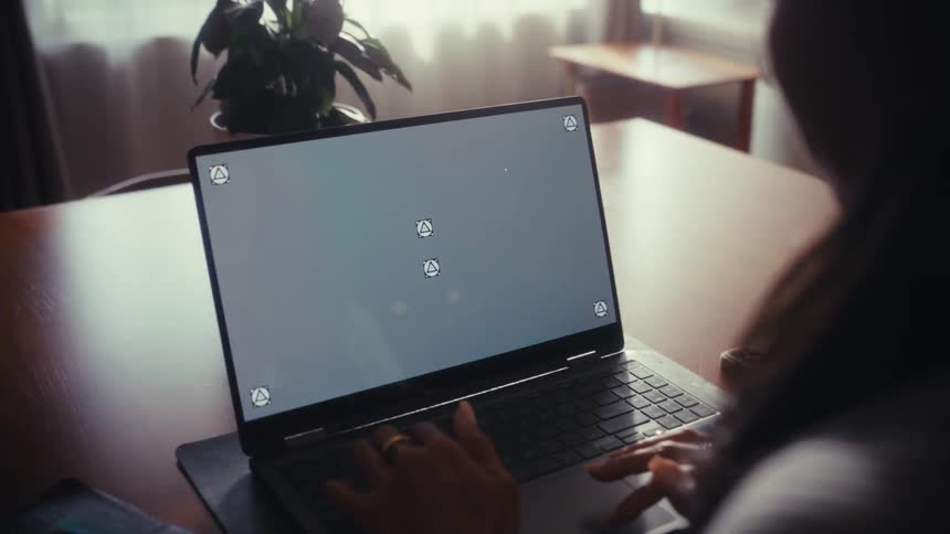 Over-the-shoulder shot of a woman typing on a laptop with a blank screen and tracking markers for screen replacement
