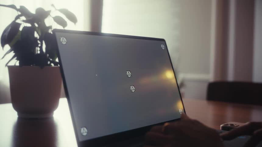 A slow push-in shot of a person working on a laptop with a trackable screen in a sunlit room