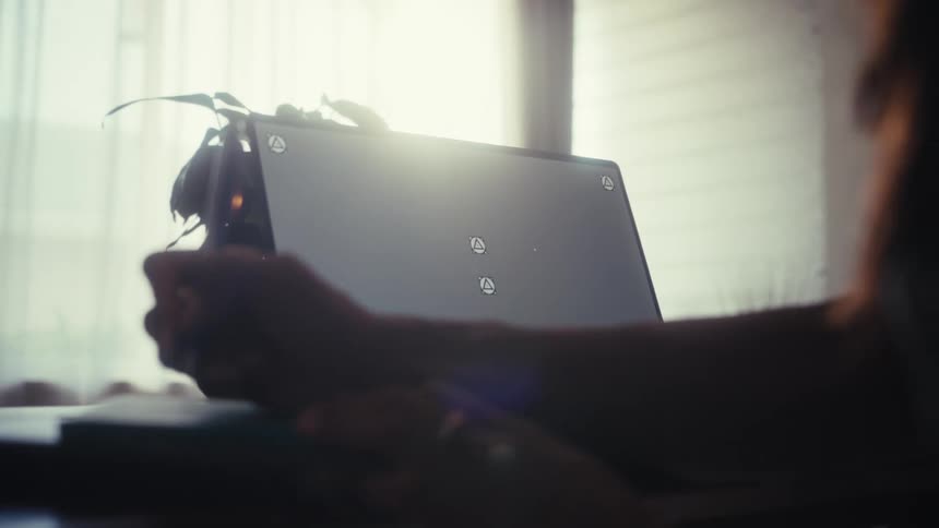 A digital artist is silhouetted as they use a stylus to draw on a tablet with a trackable screen in a sun-drenched room