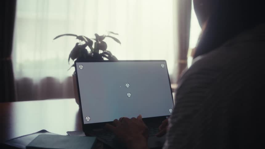 An over-the-shoulder view of a woman working on her laptop with a screen ready for content replacement in a naturally lit room
