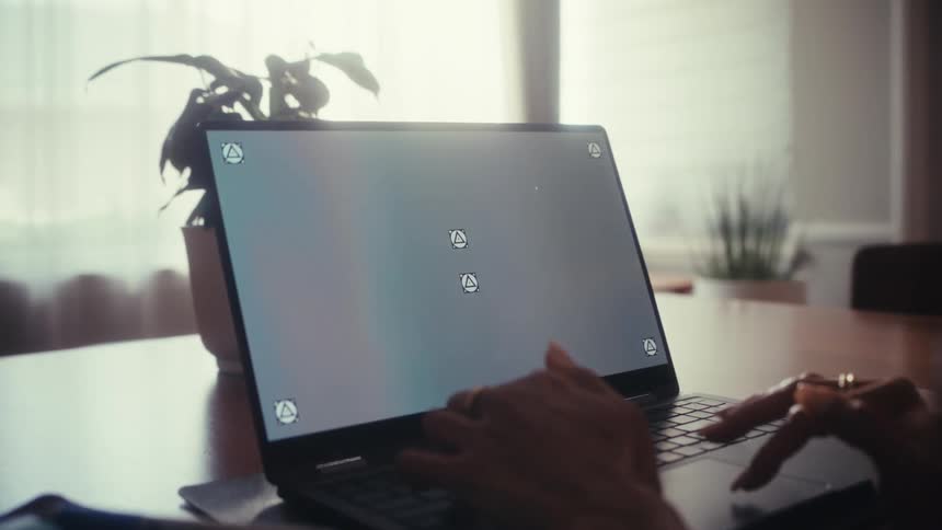 A person works on a laptop with a track-marked screen in a sunlit room as the camera slowly pushes in