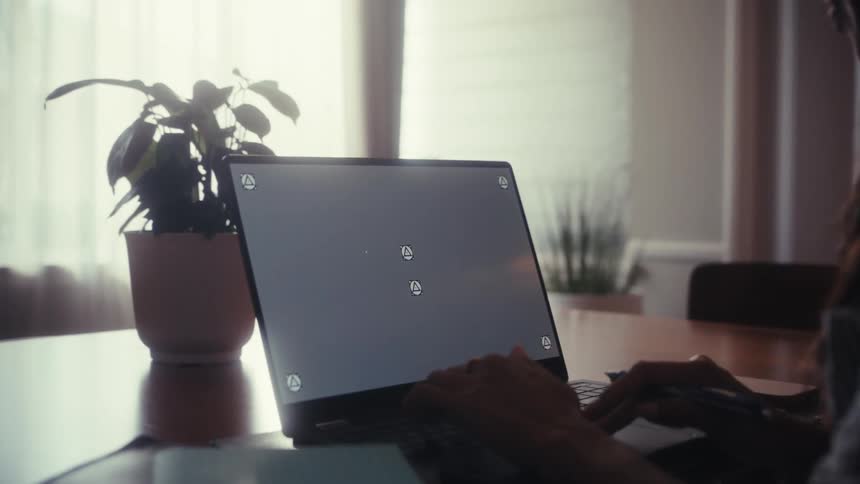 A person works from home on a convertible laptop with a blank screen, switching between using a stylus and typing on the keyboard