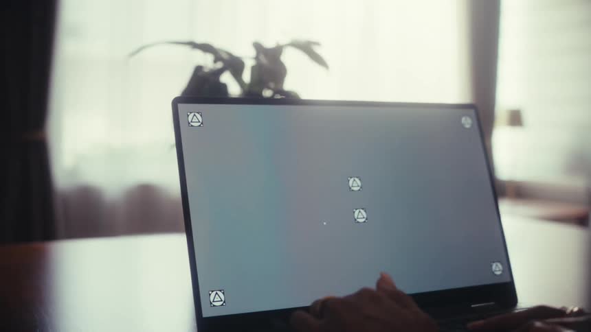 An over-the-shoulder shot of a person working on a laptop with a screen replacement template at a desk by a window