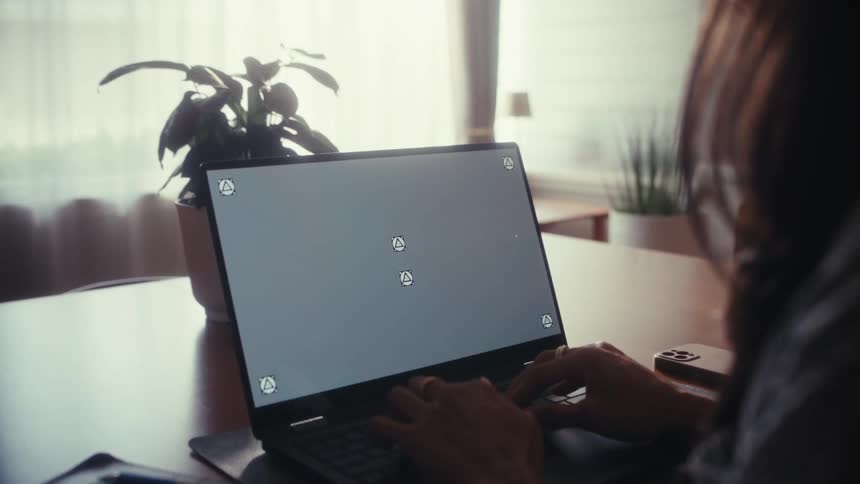 An over-the-shoulder shot of a woman typing on a laptop with a trackable screen, working from her home office