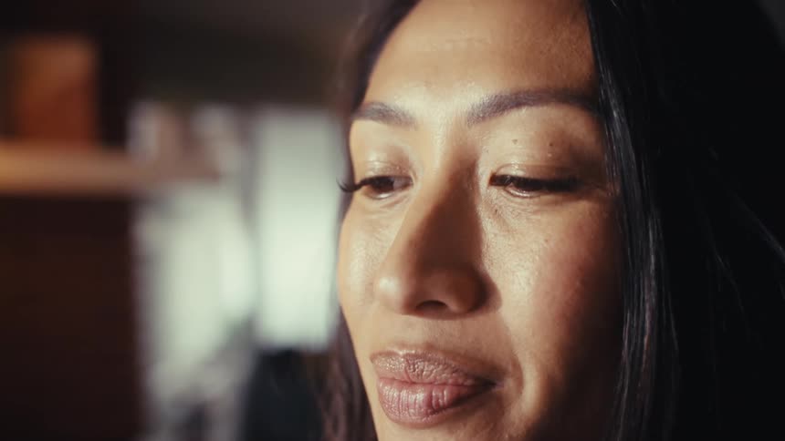 Close-up of a thoughtful woman's face transitioning to a shot of her hands typing on a laptop in a dimly lit office