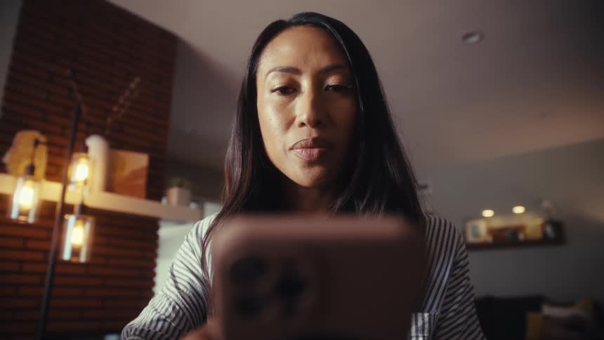 A low-angle cinemagraph shows a woman intently focused on her smartphone screen in her home