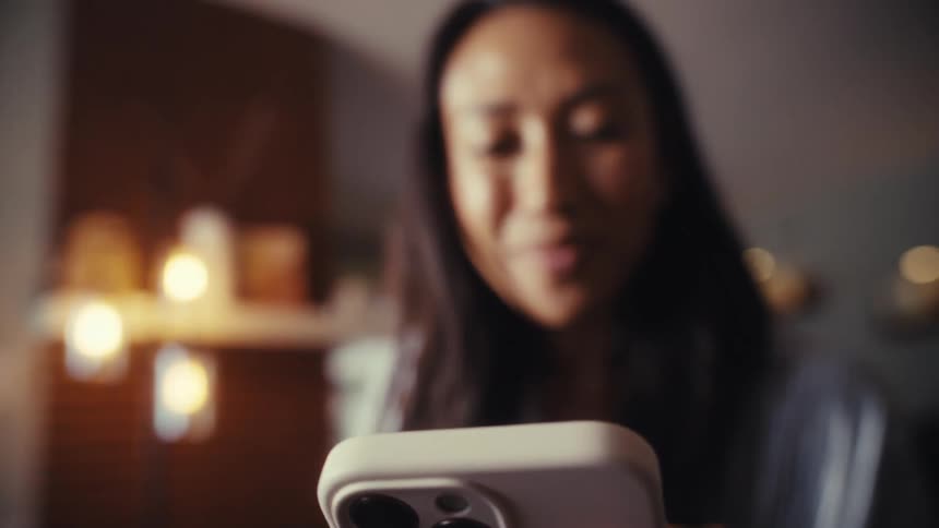 A smiling woman looks up thoughtfully from her smartphone while working in her sunlit home office