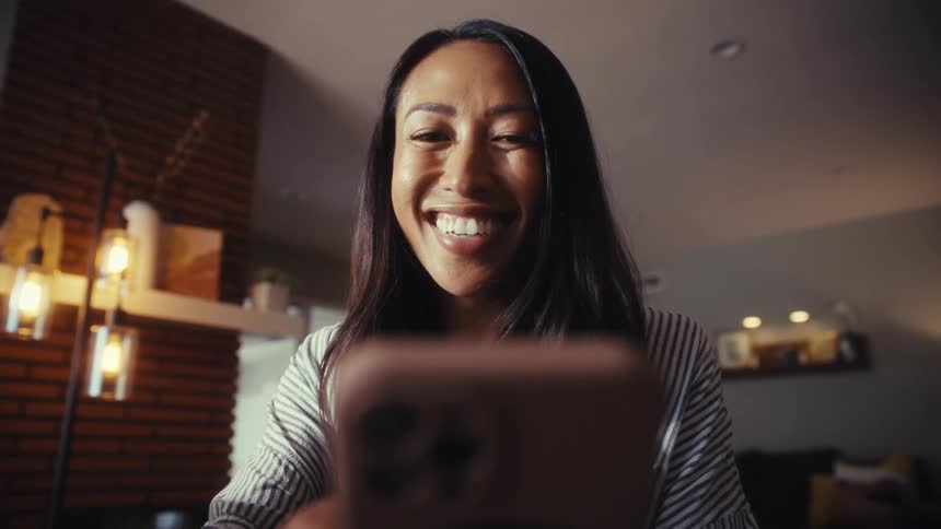 A low-angle close-up of a smiling woman looking at her smartphone in a cozy living room
