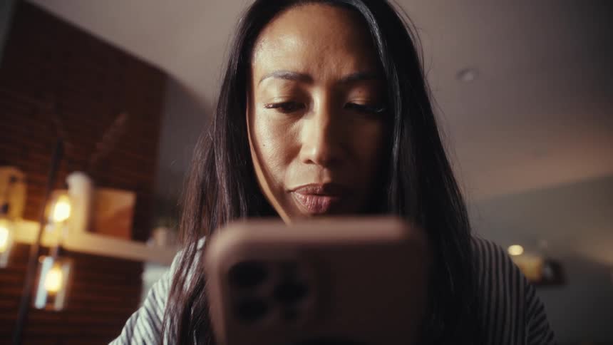 A close-up, low-angle shot of a serious woman looking down at her smartphone in her home office