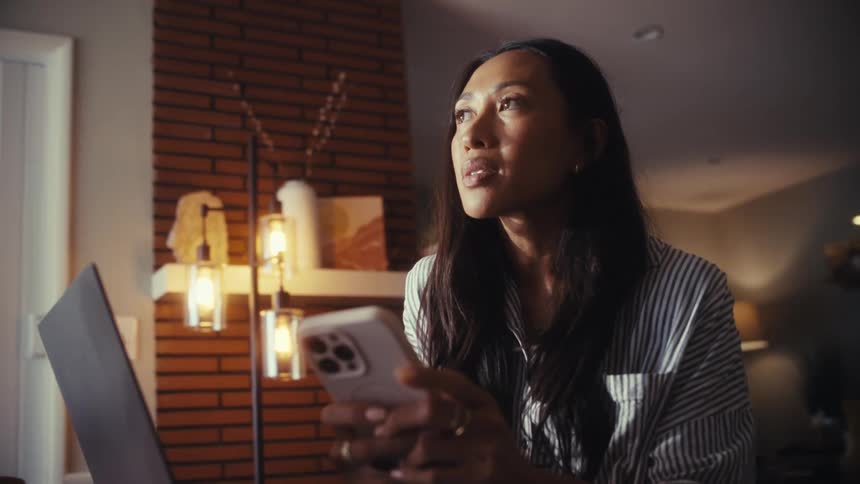 A thoughtful woman working from home reacts with sadness and tears up after reading something on her smartphone