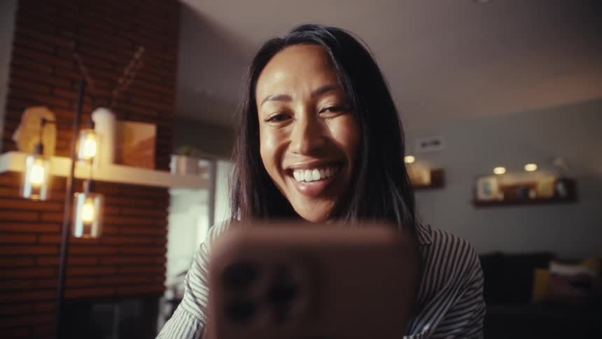 A woman's face lights up with a joyful smile and laughter while watching content on her smartphone from a low angle point of view