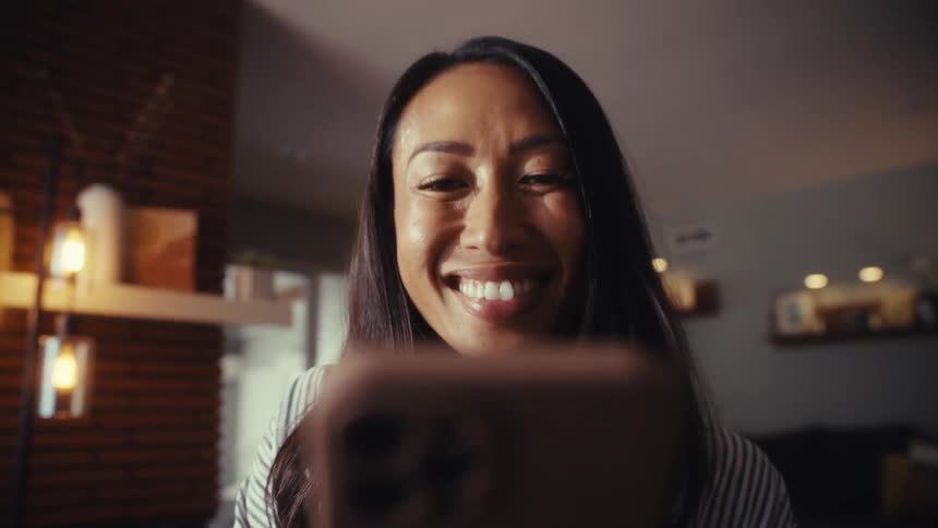 A rack focus from a blurry desk with a notebook reveals a smiling woman looking down at her smartphone