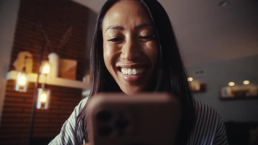 Close up low-angle shot of a woman's face as she reacts with a joyful smile to content on her smartphone