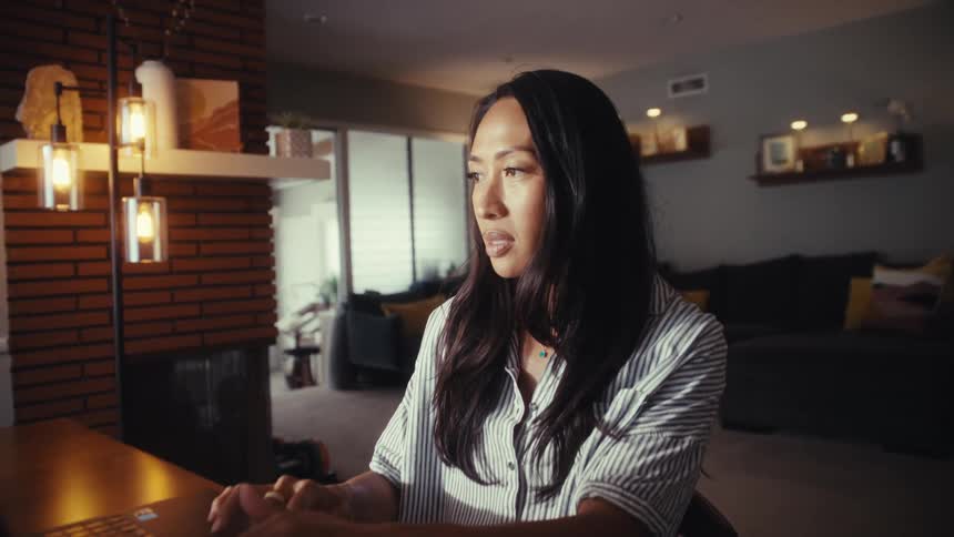 A focused woman works from her modern, warmly lit home in the evening, with the camera slowly pushing in to a close-up