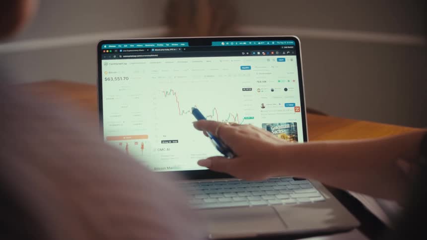 Over the shoulder shot of two people analyzing a fluctuating stock market or cryptocurrency chart on a laptop screen