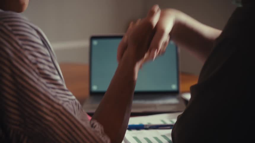 Two business partners close a deal with a handshake after reviewing information on a laptop with a green screen