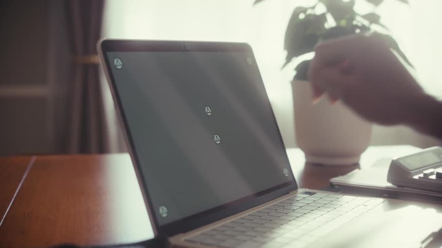 A person's hand interacts with a laptop's trackable touch screen using a finger and a pen at a sunlit desk