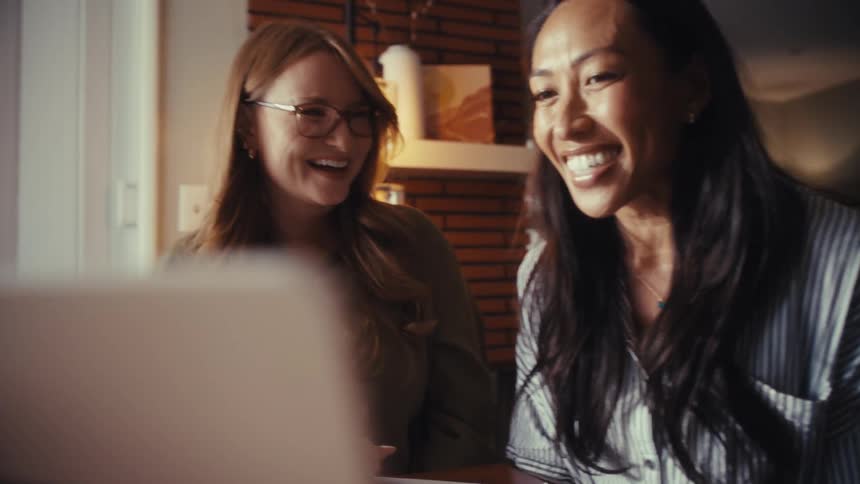 Slow motion shot of two happy businesswomen smiling and laughing while looking at a laptop screen together