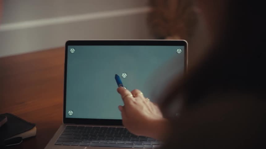 Over the shoulder shot of two people collaborating while one points at a laptop's green screen with a pen