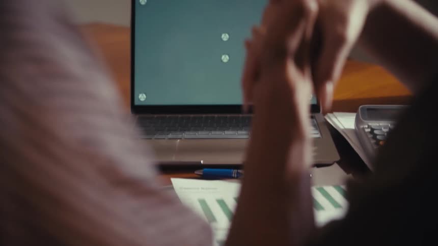 Over-the-shoulder shot of two colleagues holding hands in agreement while looking at a green screen laptop