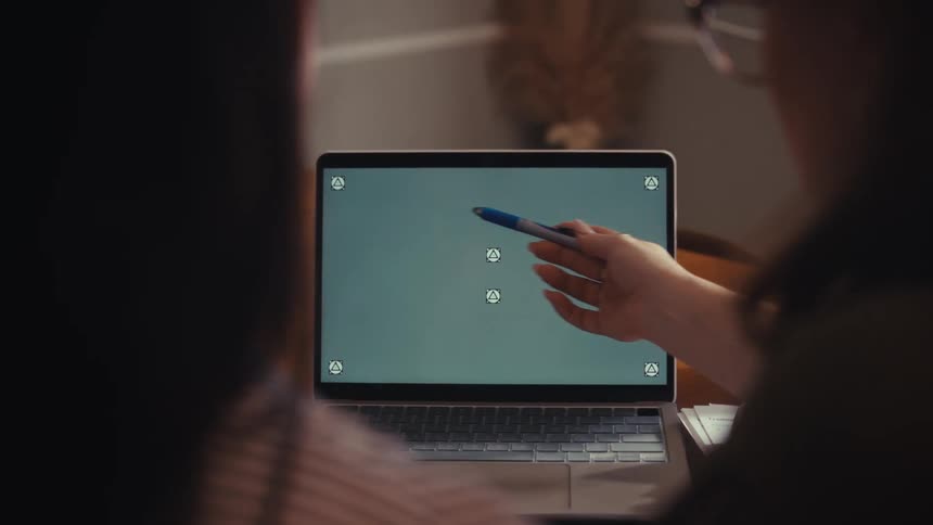 Over-the-shoulder view of a woman pointing with a pen at a laptop screen with tracking markers