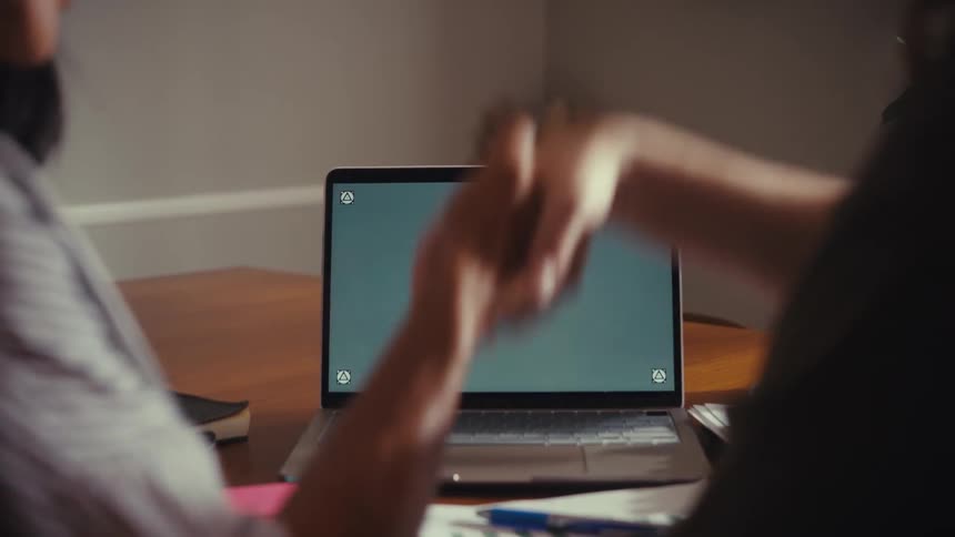 Two colleagues finalize a deal, pointing at a green screen laptop before shaking hands in a professional setting