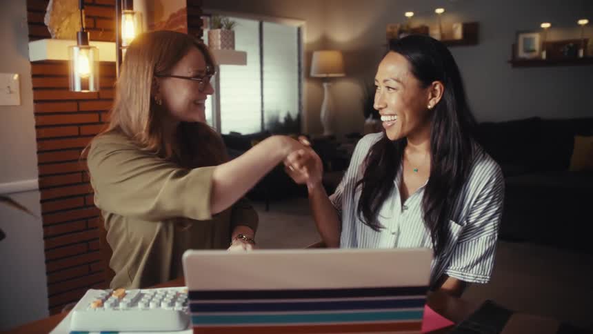 Two diverse businesswomen successfully close a deal with a happy handshake after a productive meeting with a laptop at home
