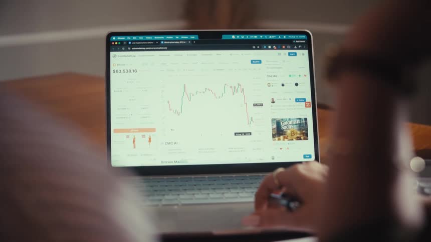 Over-the-shoulder view of a person monitoring the Bitcoin cryptocurrency price chart on a laptop screen