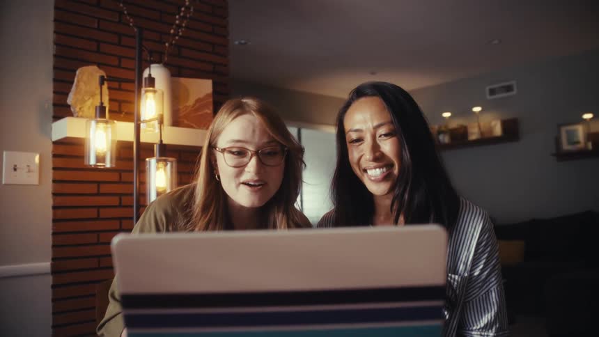 Two excited female friends share a moment of joyful surprise while collaborating on a laptop in a modern home office