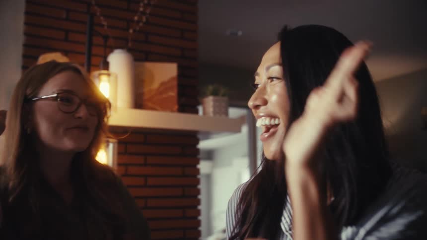 Two diverse women erupt in celebration, clapping and high-fiving in slow motion after seeing good news on their laptop