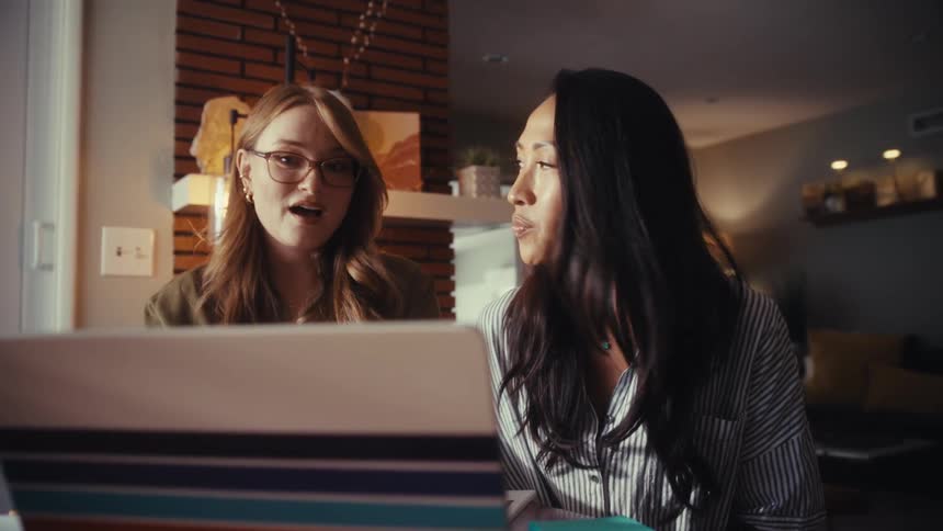 Two diverse female entrepreneurs collaborate on a laptop while working from a modern, cozy home