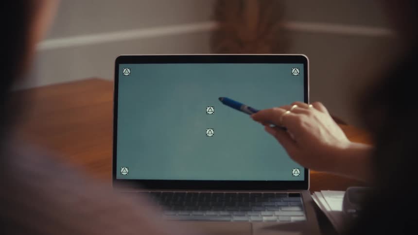 An over-the-shoulder view of two people collaborating and pointing at a laptop with a green screen and tracking markers