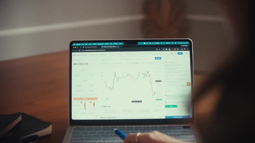 A person analyzes a cryptocurrency market graph on a laptop, using a pen to track the fluctuating data
