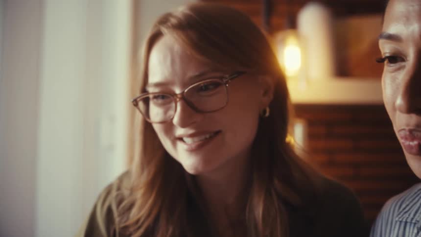 A close-up of two diverse, happy businesswomen smiling and talking while collaborating in a warmly lit office