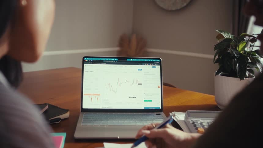 Two women analyze investment charts on a laptop while planning their financial future from home