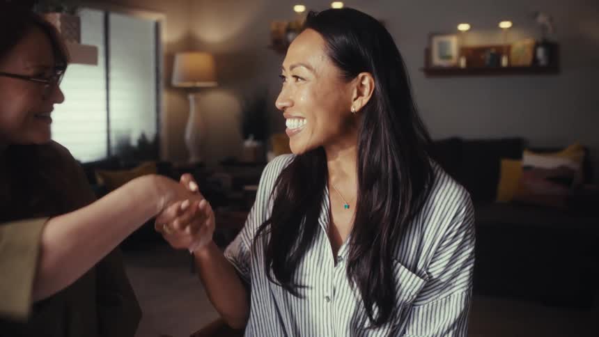 Two professional women working on a laptop at a home office smile and shake hands after reaching a successful business agreement