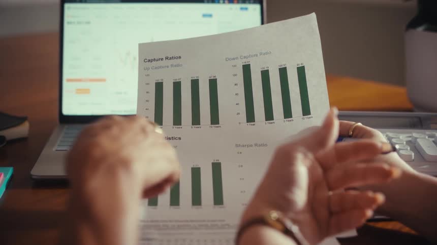 An over-the-shoulder view of two professionals discussing financial statistics and ratios on a printed bar graph report