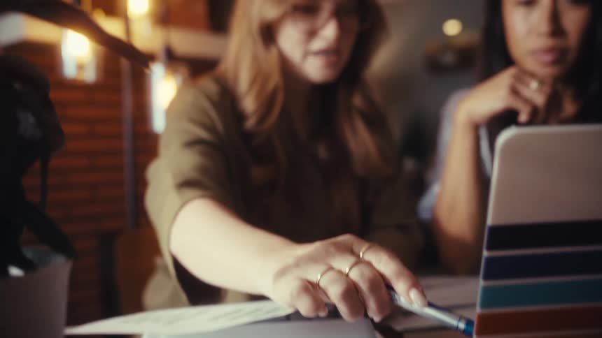 Close-up slow reveal of two diverse female entrepreneurs collaborating on a business project using a laptop in a modern office