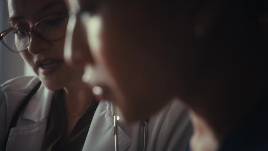 A dramatic close-up of two female doctors collaborating as they discuss important medical information in a warmly lit room