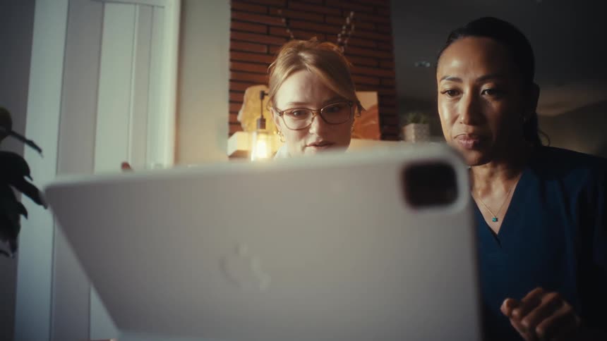A smiling female doctor and her nurse colleague collaborate on a patient's case using a tablet in their office