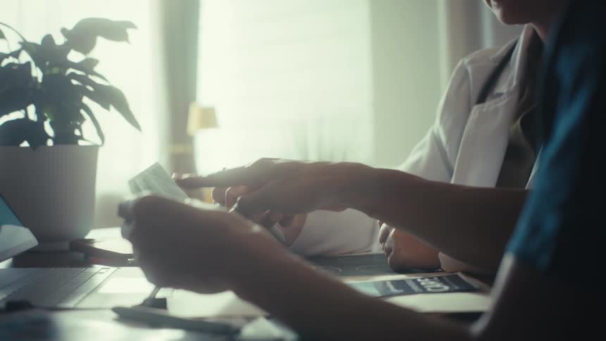 Slow-motion close-up of a doctor and nurse examining medical records together in a sunlit office