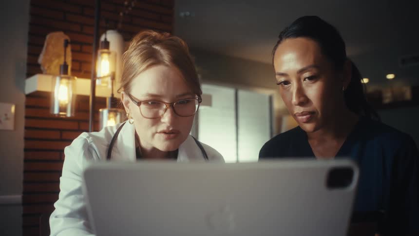 A doctor and a nurse collaborate in a modern office, seriously discussing information on a digital tablet