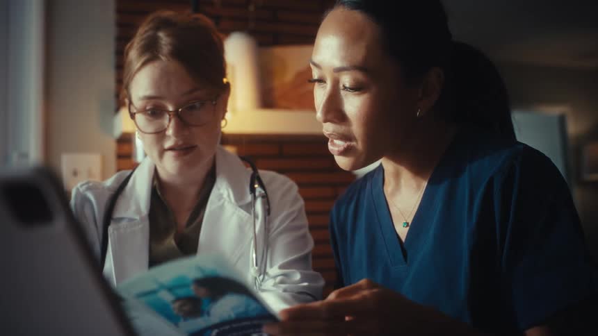 Two dedicated female healthcare professionals, a doctor and a nurse, work late in their office, collaborating over a medical brochure