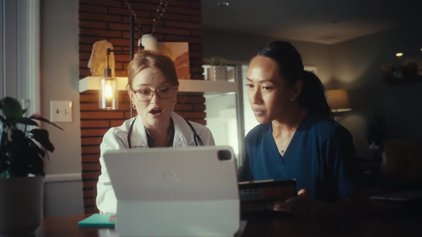 A female doctor and nurse review patient information together on a tablet in a sunlit room