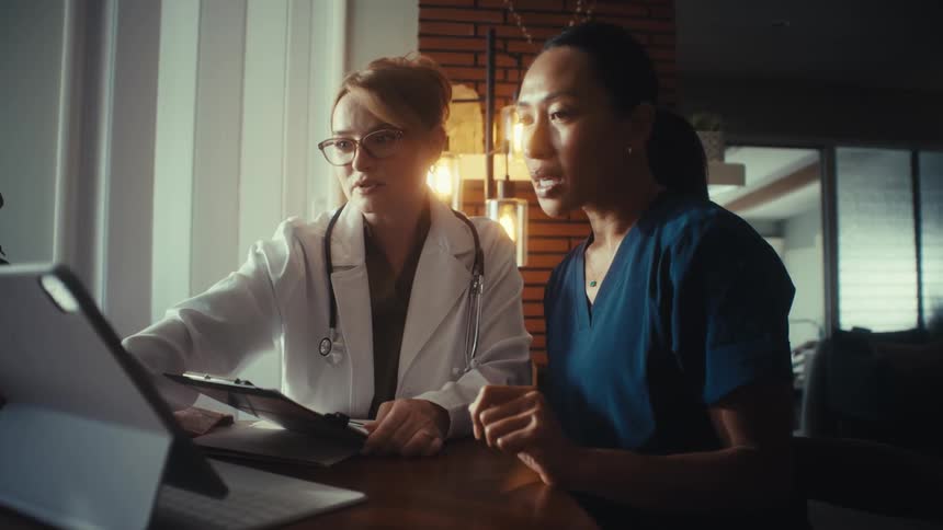 A doctor and nurse collaborate while reviewing patient information on a digital tablet in a modern office