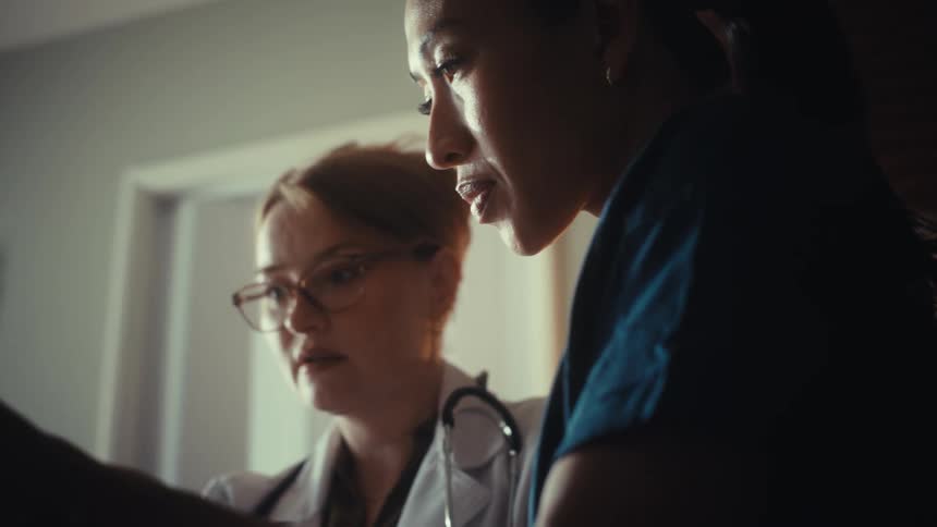 Close up of a doctor and nurse collaborating on a patient's diagnosis in a dark hospital room
