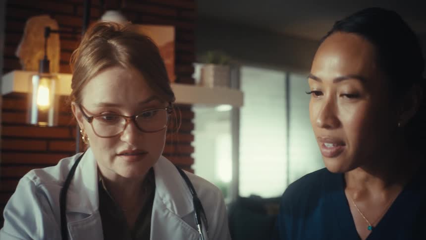 A doctor and a nurse collaborate while looking at a tablet in a medical office, discussing a patient's case