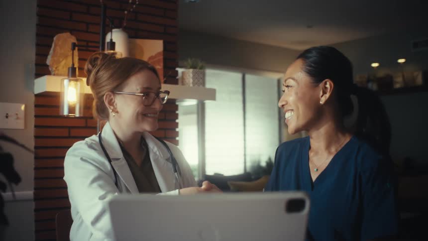 A female doctor and nurse review information on a tablet before smiling and shaking hands in agreement
