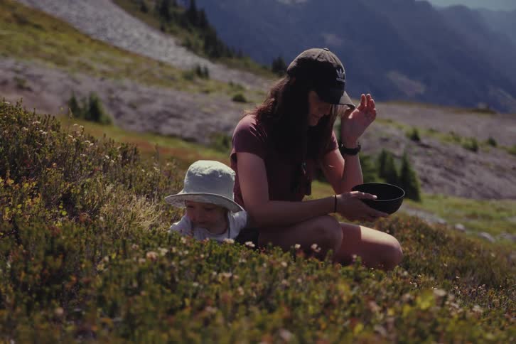 A mother and her young child forage for wild berries on a sunny day in a beautiful mountain meadow