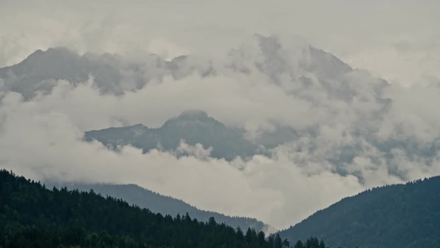 Thick fog and clouds envelop a majestic mountain range creating a moody and atmospheric scene